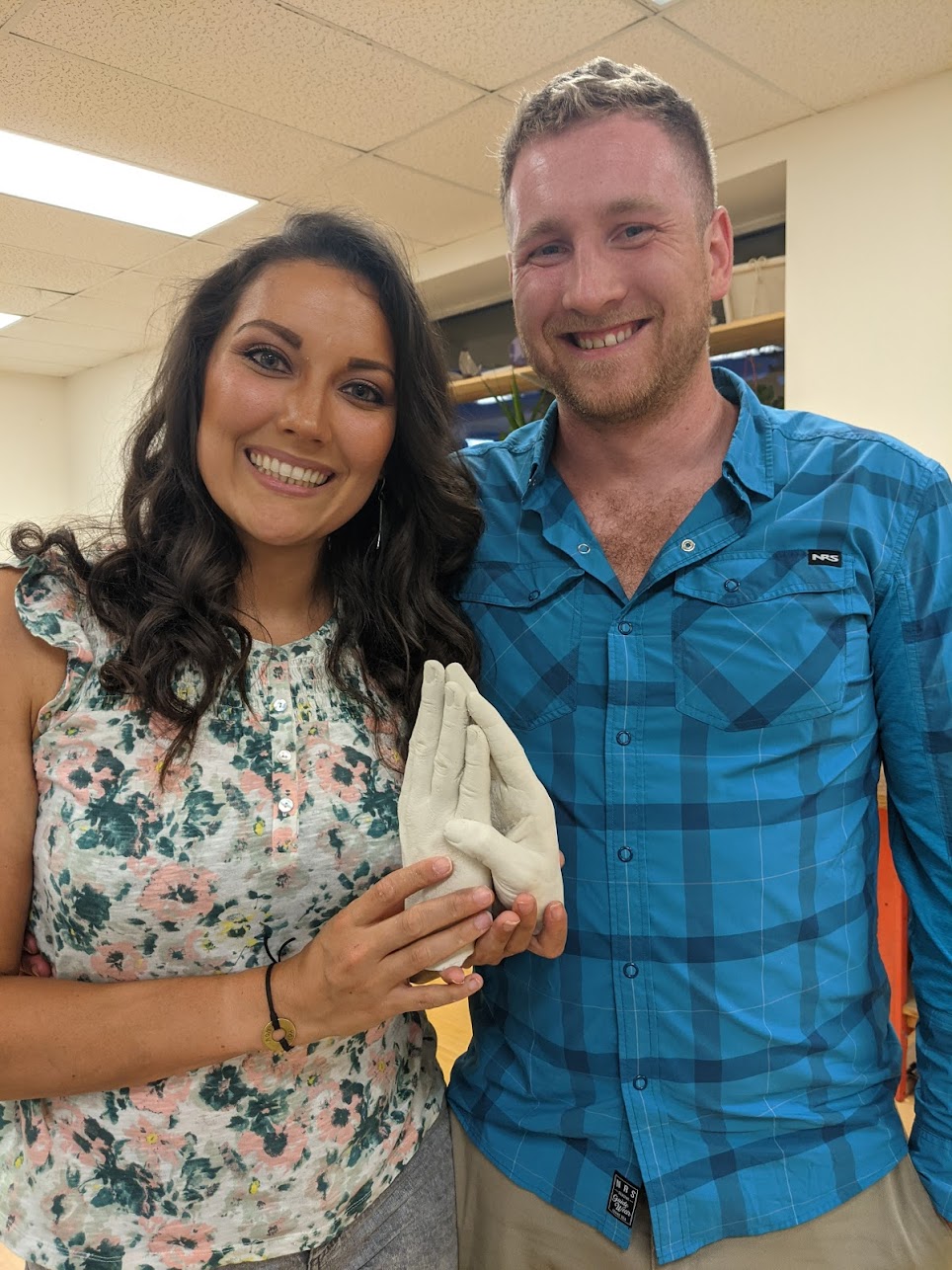 A man and woman smile while holding a plaster casting of their hands
