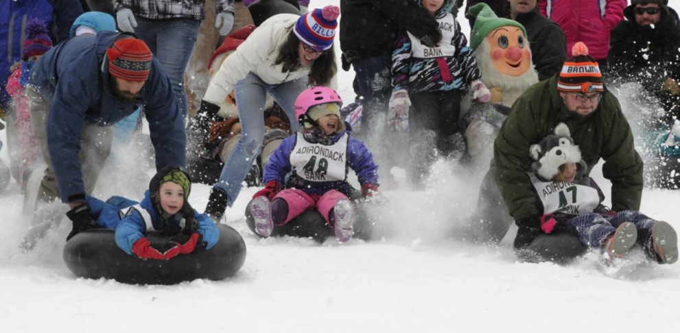 Sledders young and old race in powdery snow on tubes.