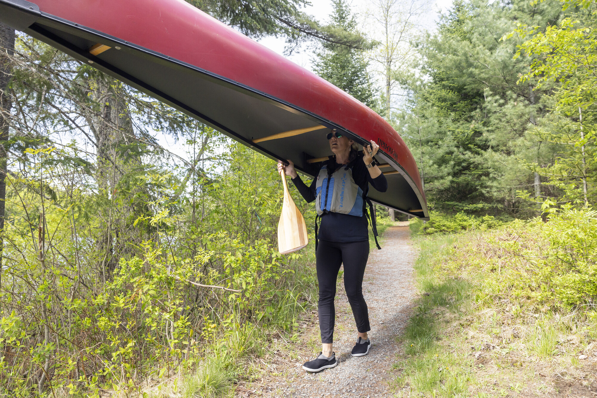 A woman carries a canoe over her head.