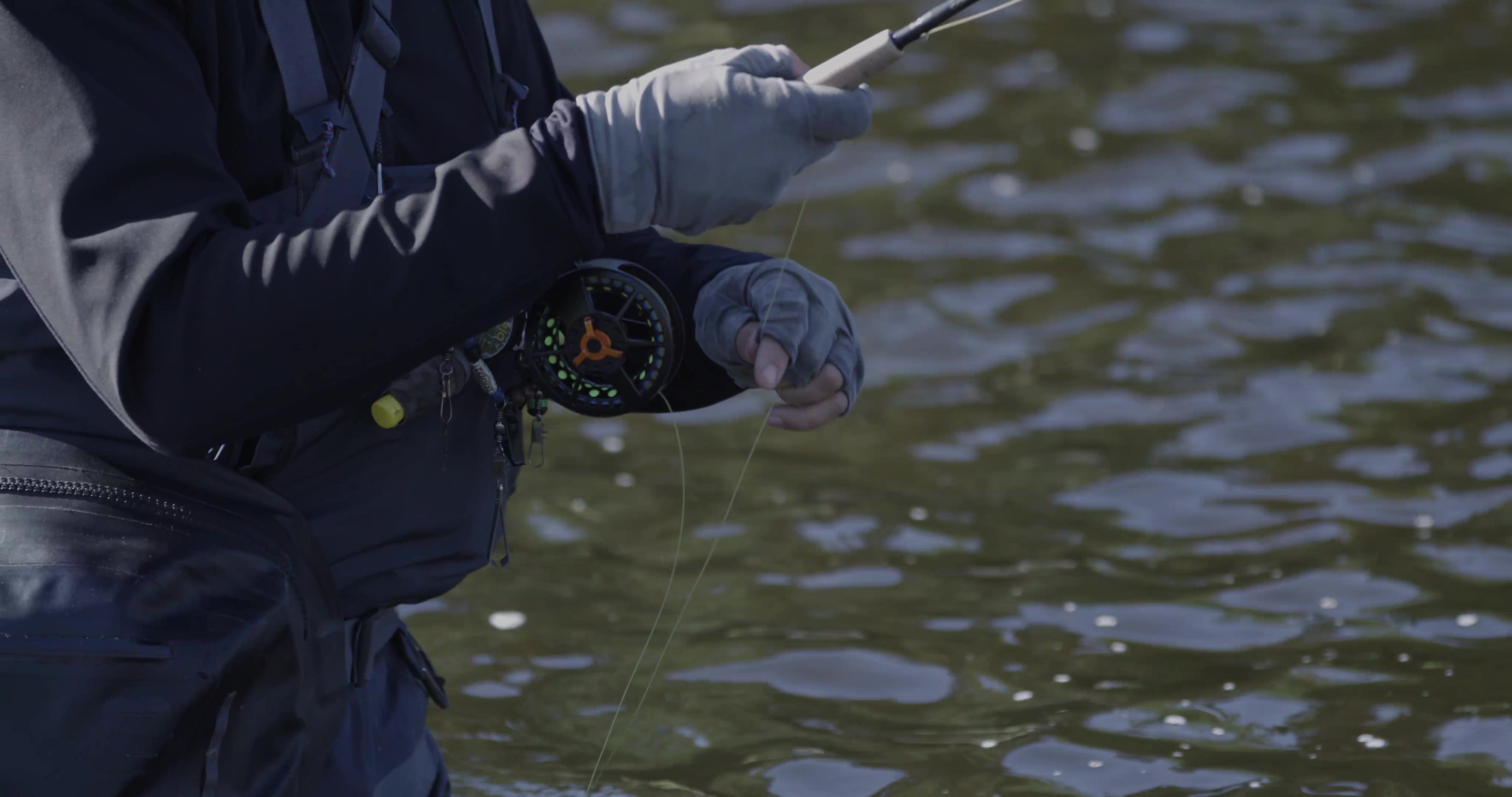 A close up of Bottcher's gloved hands as they slowly reel in his line.